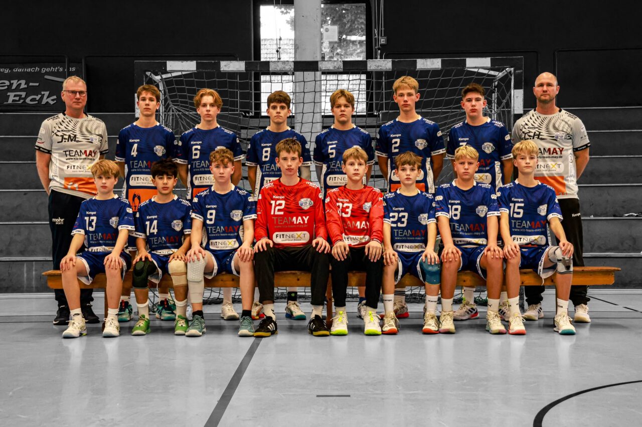 Männliche C-Jugend Handballmannschaft mit Trainern im Trikot, Mannschaftsfoto in der Sporthalle vor dem Handballtor.